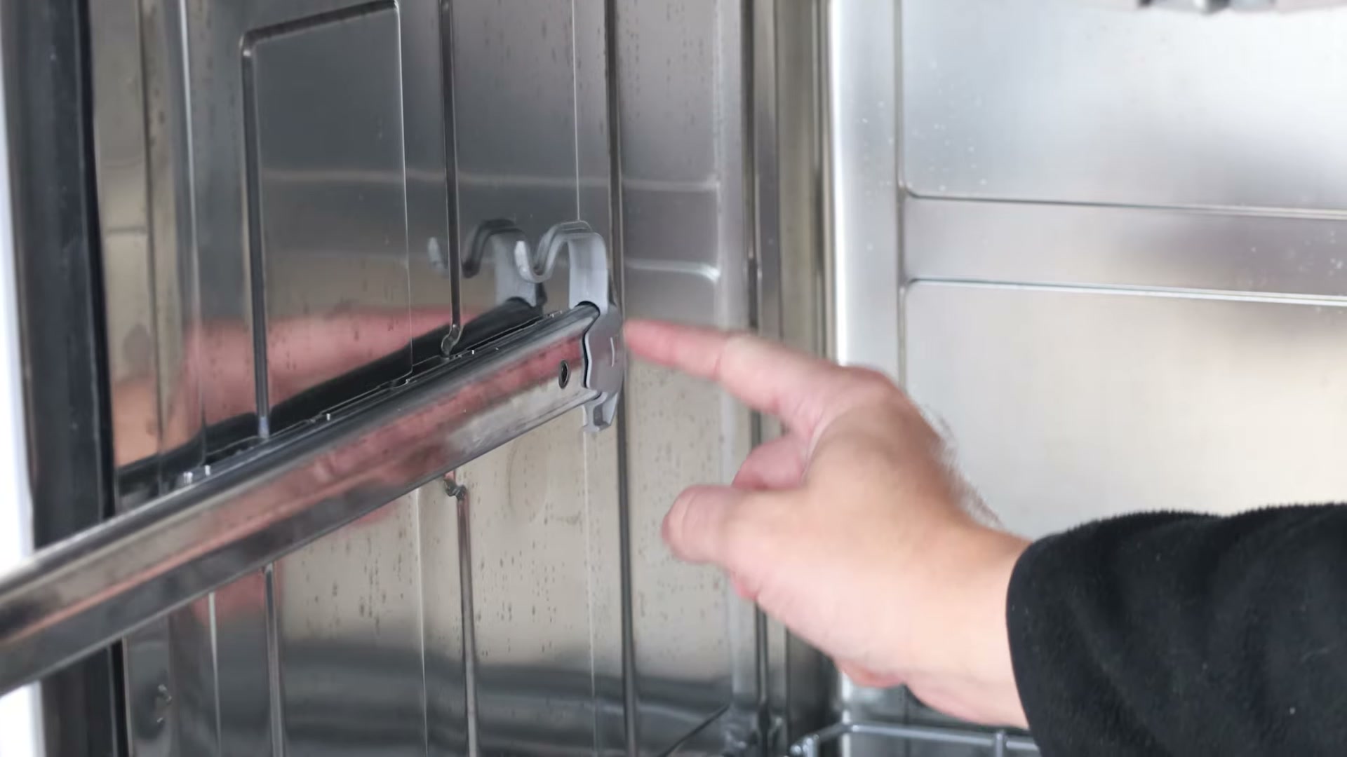 Finger pointing to the basket rail clip on the end of a Bosch dishwasher side rail