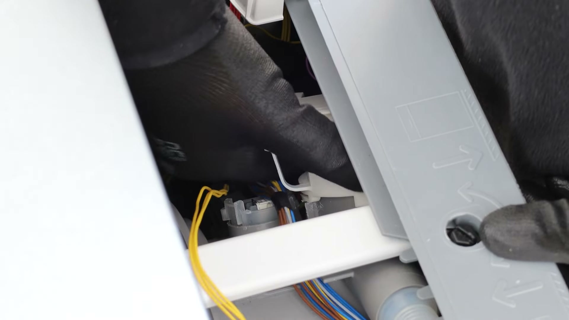 Flat-head screwdriver pressing down the mounting tab to rotate the old drain pump out of a Bosch dishwasher