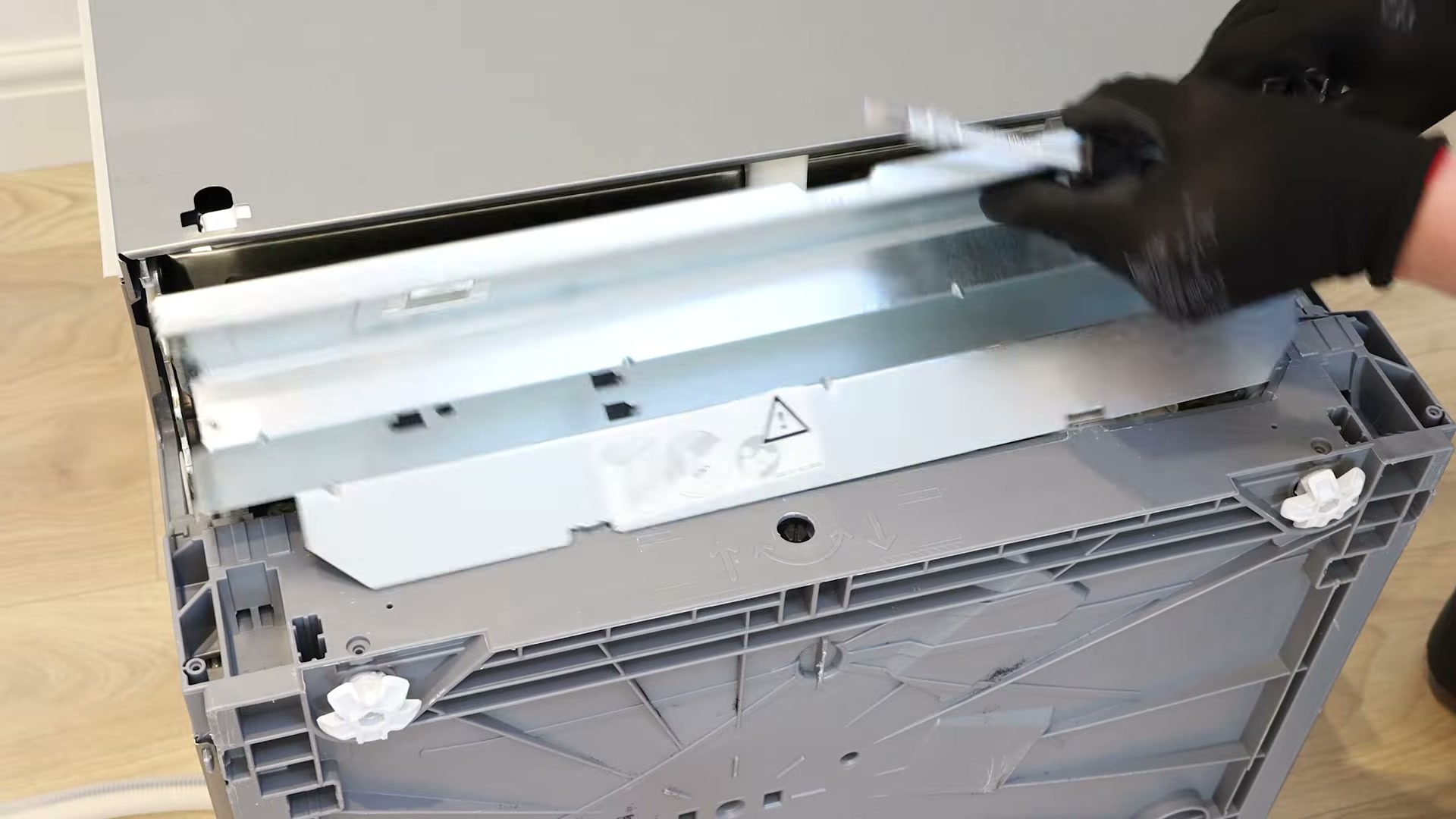 Kick plate being lifted away from the base of a Bosch dishwasher with a flat-head screwdriver
