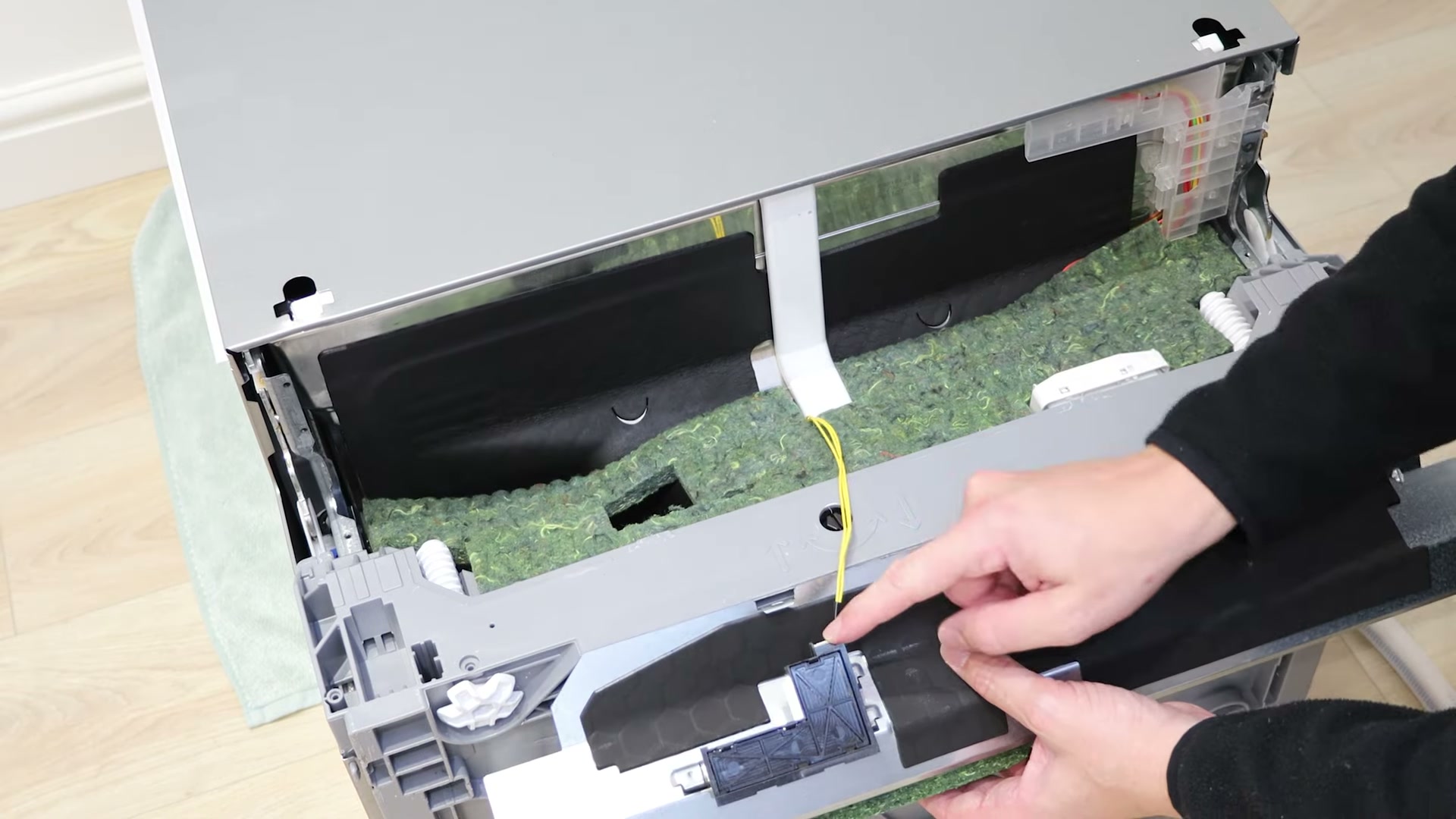 Kick plate lifted off a Bosch dishwasher showing the insulation and floor time light connector
