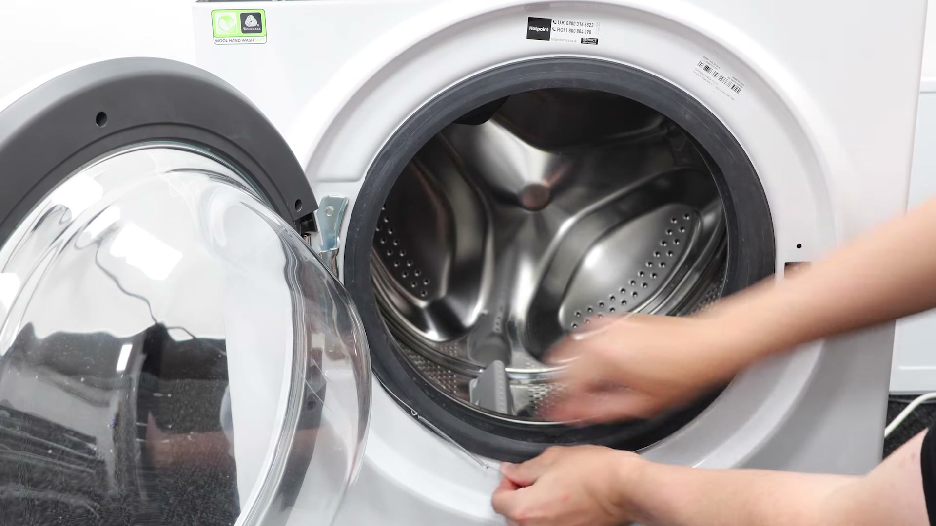 Hands refitting the outer clamping band ring spring onto the new door seal of a Hotpoint washing machine