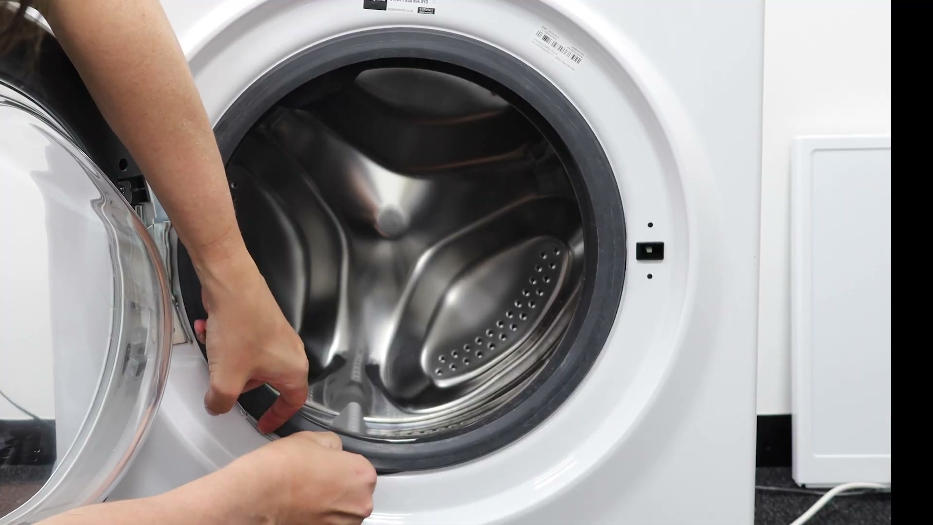 Flat-head screwdriver being used to lift the front outer clamping band off a Hotpoint washing machine door seal